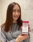 Smiling woman holding up Tint of Nature Henna Cream mahogany red semi-permanent hair dye after using the colour