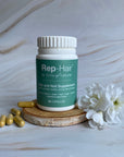 Tints of Nature Rep-hair hair and nail supplements bottle on a wooden log with a flower and supplements at the side.