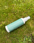 Tints of Nature Seal and Shine Leave-in Conditioner spray bottle resting on green grass outdoors.