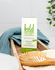 Box of Tints of Nature Bold Green hair dye displayed in a bathroom with hairbrush and towel.