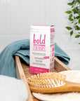 Box of Tints of Nature Bold Pink hair dye displayed in a bathroom with hairbrush and towel.