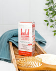 Box of Tints of Nature Bold Rose Gold hair dye displayed in a bathroom with hairbrush and towel.