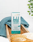 Box of Tints of Nature Bold Teal hair dye displayed in a bathroom with hairbrush and towel.